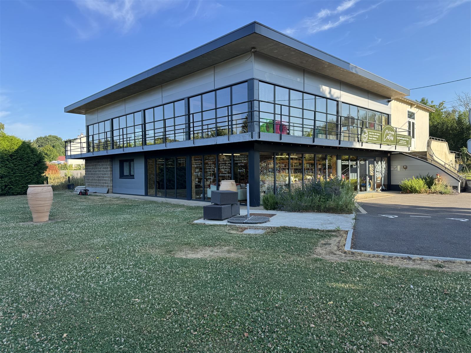 Le b&acirc;timent de la boutique vu du jardin, avec sa grande jarre cr&eacute;toise pos&eacute;e dans l'herbe